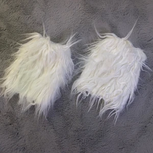 Vita pälsiga benvärmare - Säljer ett par vita benvärmare med lång, fluffig päls. Perfekta för att ge en unik och varm look till dina outfits. De är lätta att dra på över byxor eller leggings.