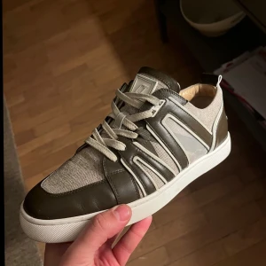 Cristian Louboutin  - En av dom mest ikoniska skorna Cristian Louboutin sneakers i brunt och beige med vita detaljer. Skorna har snörning och en vit sula. Perfekta för en stilren look. Låda och två dustbags medföljer.Kan även tänkas byta mot något kul,skick 9/10 använda ett fåtal gånger.