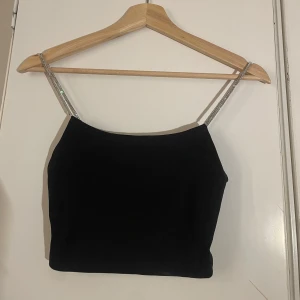 Svart linnetopp med glittriga axelband - Snygg svart linnetopp med glittriga axelband som ger en festlig touch. Perfekt för en utekväll eller speciella tillfällen. Enkel och stilren design som passar till många olika outfits.