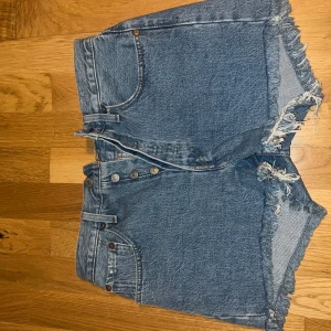 Blå jeansshorts från Levi's - Säljer ett par klassiska blå jeansshorts från Levi's med fransiga kanter och knappgylf. Perfekta för en avslappnad stil. Oanvänt Levi’s shorts 501 utan tagg. Mellanhög midja. Har inte använt dessa pga jag köpte fel storlek. Dessa är W26