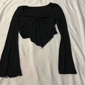 Svart långärmad topp - Snygg svart långärmad topp med unik design och lätt utsvängda ärmar. Toppen har en elegant drapering framtill som ger en stilfull look. Perfekt för att lyfta vilken outfit som helst.