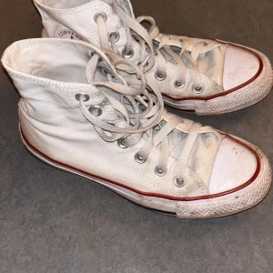 Converse skor - Klassiska vita höga sneakers från Converse med snörning och den ikoniska loggan på sidan. Skorna har en röd rand längs sulan och är perfekta för en avslappnad stil. De är smutsiga och trasig som converse brukar bli! 