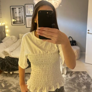 Vit smockad topp från H&M - Säljer en vit smockad topp från H&M med trekvartsärmar och volangdetalj vid nederkanten💕