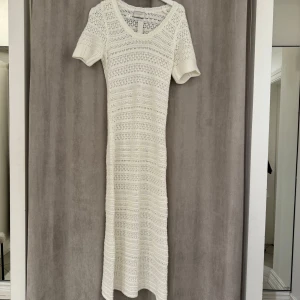 Neo noir klänning - Säljer en elegant vit stickad klänning från Neo Noir. Klänningen har en v-ringad design och korta ärmar, perfekt för en stilren look. Den är i en lång modell och har ett vackert stickat mönster som ger en unik touch.