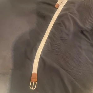 Beige flätat bälte med bruna detaljer - Snyggt beige flätat bälte med bruna skinn-detaljer och en stilren silverfärgad spänne. Perfekt för att ge en avslappnad men ändå stilren touch till din outfit.