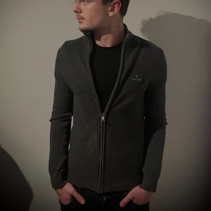 Grå kofta från Gant - Snygg grå kofta från Gant med dragkedja framtill. Perfekt för lager-på-lager och har en stilren design med ribbade muddar. Passar både till vardags och mer uppklädda tillfällen.