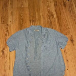 Blå linneskjorta från Dressmann - Säljer en stilren blå skjorta från Dressmann i linneblandning. Skjortan har korta ärmar och knappar framtill. Kontakta vid frågor. 