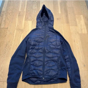 Mörkblå peak perfomance hybrid javka - Snygg mörkblå jacka med quiltad design och huva. Jackan har dragkedja framtill och långa ärmar. Perfekt för kyligare dagar.