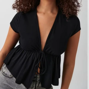 Svart v-ringad topp från Gina tricot  - Snygg svart topp med v-ringning och korta ärmar. Den har en knytning framtill🤩