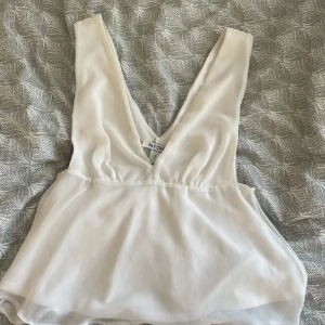 Vit topp - Säljer en stilren vit topp från nly one med djup v-ringning. Perfekt för varma dagar eller som en del av en lager-på-lager look. Toppen har en luftig passform och är tillverkad i ett lätt material.