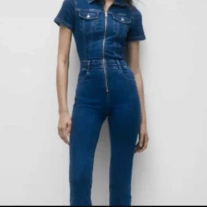 Pull & Bear jeans jumpsuit  - Trendig mörkblå jeans jumpsuit med korta ärmar och dragkedja framtill. Den har en högmidjad passform och klassisk krage. Perfekt för en stilren look.