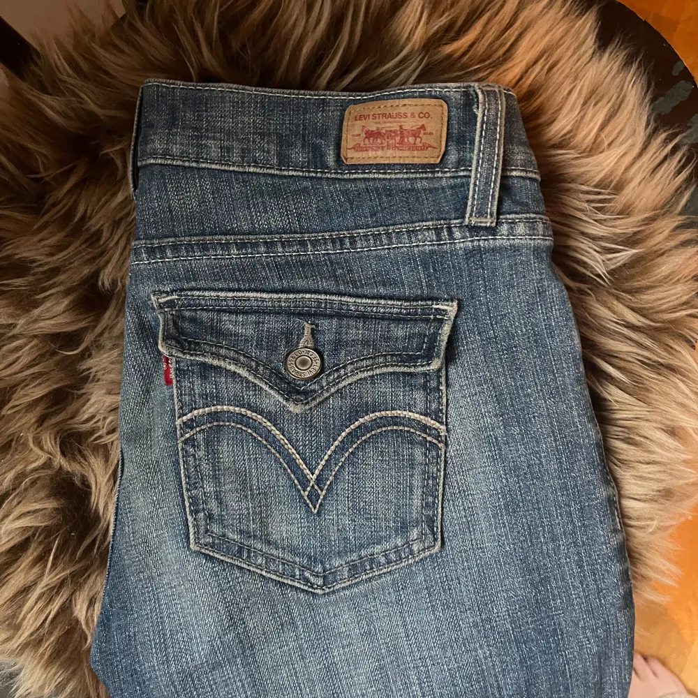 Snygga blå bootcut jeans från Levi's med klassisk femficksdesign och knappgylf. Jeansen har en lätt slitning för en avslappnad look och är perfekta för en casual stil. Levi's logotyp syns på bakfickan. Köpta i Paris för ca 2 år sedan och inga slitningar eller skador. Storlek 36/38. Farkut & Housut.