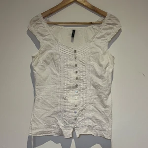 Vit blus från Soya - Söt vit blus från Soya med knappar framtill och ett diskret prickigt mönster. Blusen har korta ärmar och fina spetsdetaljer längs knappraden.