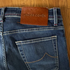 Blå jeans från Jacob Cohën - Helt nya! Klisterlappar inuti jeansen sitter kvar, doftar Jacob Cohens signatur parfym.   Nypris 6000 svenska kronor. Säljer för 2345kr.   Storlek 31.  Följande mått Midja: ca 41 cm Innerbens längd: ca 73 cm Ben öppning: ca 17 cm  Kom endast med seriösa bud!  Vid frågor skriv privat