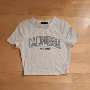 Vit croppad t-shirt med tryck - Säljer en vit croppad t-shirt med texten 'California West Coast' tryckt på framsidan. Perfekt för en avslappnad stil. Kortärmad, bekväm och figurnära t-shirt att bära nu till sommaren. 🤍🤍