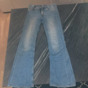 Blå jeans från Kappahl - Säljer ett par klassiska blå jeans från Kappahl i storlek 152. De har en bootcut-stil och är perfekta för en avslappnad look. Jeansen har en dragkedja och knapp framtill.