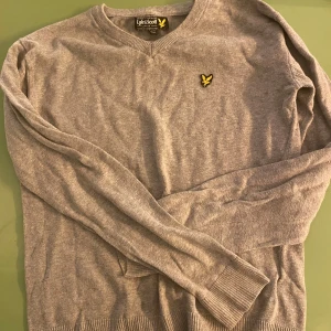 Grå tröja från Lyle & Scott - Jag Säljer en stilren grå tröja från Lyle & Scott med v-ringning och deras ikoniska gula logga på bröstet. Tröjan har långa ärmar och ribbade muddar, perfekt för en avslappnad look. 9/10 skick