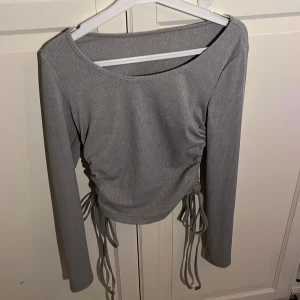 Grå långärmad topp  - Har aldrig använt. Man han dra i snörerna för att ljustera hur lång tröja ska vara. Man kan knyta på sidan också. Men har klippt av lappen där bak.