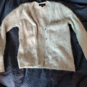 Grå kofta  - Mysig grå kofta i fluffigt material. Den har en v-ringad design med knappar framtill. Perfekt för kyliga dagar.