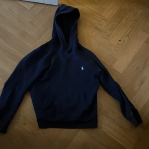 Mörkblå hoodie från Ralph Lauren - Säljer en stilren mörkblå hoodie från Ralph Lauren med den klassiska loggan på bröstet. Tröjan har långa ärmar och en bekväm huva. Perfekt för en avslappnad look. Tröjan är i barnstorlek