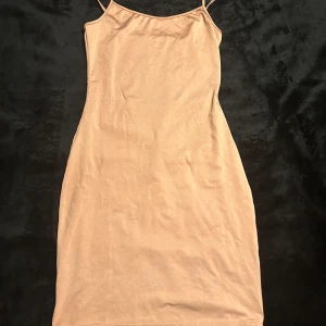 Beige klänning från Shein - Snygg beige kort klänning från Shein med smala axelband. Perfekt för en stilren look. Klänningen har en enkel design som gör den lätt att matcha med olika accessoarer.