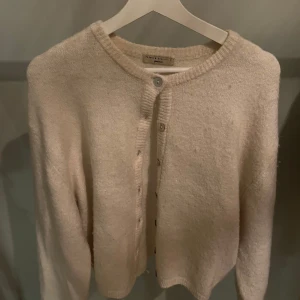Beige kofta från Gina Tricot - Mysig beige kofta från Gina Tricot i premiumkvalitet. Den har knappar framtill och långa ärmar, perfekt för kyliga dagar. Enkel och stilren design som passar till det mesta.
