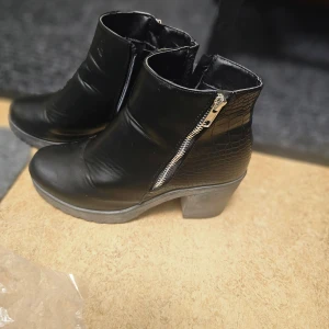 Svarta boots med dragkedja - Snygga svarta boots med dragkedja och klack. Skorna har en krokodilpräglad textur på sidorna som ger en extra touch. Perfekta för höst och vinter.