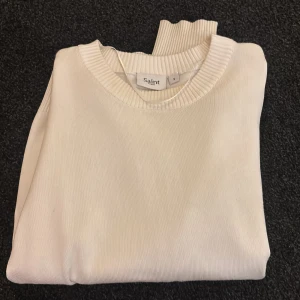 Vit tröja från Saint - Säljer en stilren vit tröja från Saint. Tröjan har en rund halsringning och långa ärmar,  tyvärr är det smuts på armen som syns på andra bilden men inget som uppmärksammars och skriv ifall du har fler frågor 