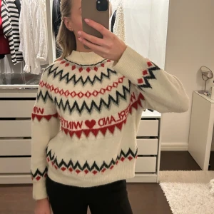 Vit stickad tröja med mönster - Säljer en mysig vit stickad tröja med rött och svart mönster. Tröjan har långa ärmar och ett klassiskt vintermotiv med hjärtan och text. Perfekt för kyliga dagar! 