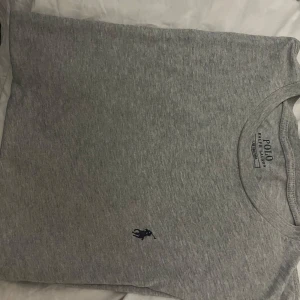 Grå t-shirt från Polo Ralph Lauren - Snygg grå t-shirt från Polo Ralph Lauren med klassisk passform. Den har en liten broderad logga på bröstet. Perfekt för en avslappnad stil.