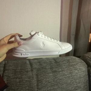 Vita sneakers från Polo Ralph Laurent  - Snygga vita sneakers från Polo med klassisk design och snörning. Skorna har en diskret logga på sidan och en bekväm sula. Perfekta för en stilren look.