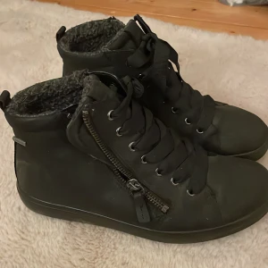 Svarta boots med dragkedja och snörning  - Säljer ett par svarta boots med både snörning och dragkedja. De har en varm, fodrad insida som passar perfekt för kyligare dagar. Skorna är stilrena och praktiska med en robust sula.