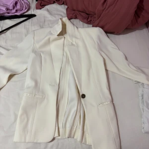 Vit kavaj med knappar - Elegant vit kavaj med stilrena knappar och klassisk design. Perfekt för en chic look. Långärmad med en knapp framtill och tre dekorativa knappar vid ärmslutet.