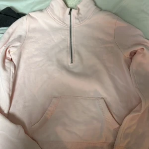 Rosa fleecefodrad tröja från Hollister - Mysig rosa tröja från Hollister med fleecefoder och halv dragkedja. Perfekt för kyliga dagar med sin varma insida och praktiska ficka framtill. Tröjan har långa ärmar och en hög krage.