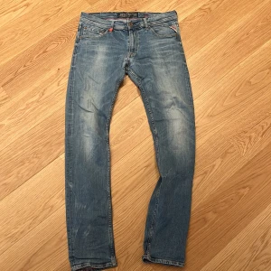 Blå Replay Jondrill jeans - Säljer ett par snygga blå Replay Jondrill jeans med en klassisk femficksdesign och knappgylf. Jeansen har en modern slim passform och är perfekta för en avslappnad stil. De har en lätt tvättad look med subtila slitningar för en trendig touch.
