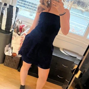 Mörkblå glittrig  axelbandslös klänning - Snygg mörkblå axelbandslös klänning med volangdetaljer. Perfekt för en kväll ute eller en speciell tillställning som t.ex nyår. Klänningen har en kort längd och en elegant passform. Volangdelen är av tre lager och det finns ett svart innertyg så att klänningen är bekväm och inte skaver av glittret. Skulle säga storlek S-M. Tyget är från Ohlssons tyger och själva klänningen har jag sytt själv.