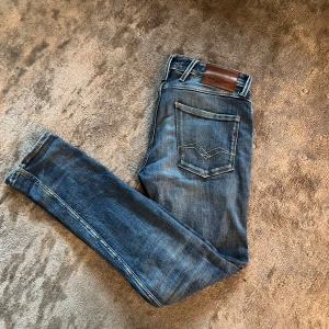Slitna Replay blåa (anbass) - Snygga blå jeans från Replay i en klassisk stil med slitna detaljer. Tillverkade av hållbar bomull, dessa jeans har en normal passform och är perfekta för en avslappnad look. De har en traditionell femficksdesign och en läderdetalj vid midjan.🎧