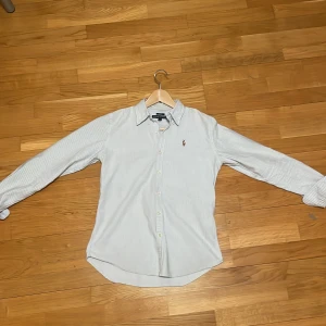 Randig skjorta från Ralph Lauren - Blå och vit- randig skjorta från Ralph Lauren med broderad logo. Det är slim fit. Säljs pågrund av att den inte passar längre. Övrigt en snygg skjorta som passar till allt pris kan diskuteras.HAR ANDRA FÄRGER⚪️🔵kolla mitt konto. Byten är intressanta.