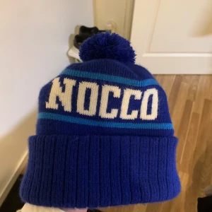 Blå mössa med tofs från NOCCO - SÄLLSYNT snygg marinblå mössa med stor tofs och NOCCO-logga i vitt. Mössan har ribbad kant och är perfekt för nu i vinter. Går ej att få tag på utan måste fås direkt från nocco själva och därav sällsyntheten. Värde kring 1000kr men säljer nu för endast 699.