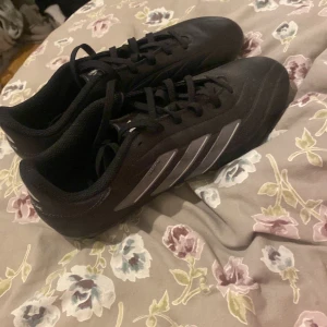 Svarta Adidas Copa Pure fotbollsskor - Säljer ett par svarta Adidas Copa Pure fotbollsskor med vita dobbar och de klassiska tre ränderna i silver på sidan. Skorna har snörning och är perfekta för fotbollsspel på gräs. Dem är helt oanvända 