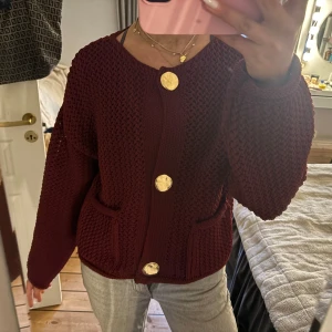 Vinröd stickad kofta med stora knappar - Säljer en mysig vinröd stickad kofta med stora guldknappar. Koftan har en grovstickad textur och två fickor framtill. Aldrig använd 😊💓💓