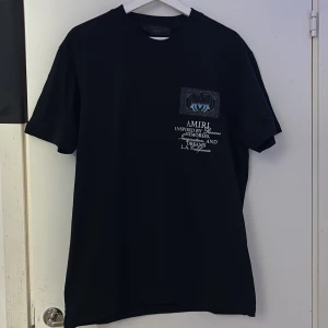 Svart t-shirt från Amiri - Snygg svart t-shirt från Amiri med tryck i blått och vitt på både fram- och baksidan. T-shirten har en normal passform och korta ärmar. Perfekt för en avslappnad stil med en touch av lyx.