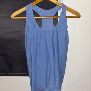 Blå linnetopp - Säljer en blå linnetopp i polyester och nylon. Toppen har en sportig design med brottarrygg och är perfekt för träning. Materialet är lätt och andas bra.