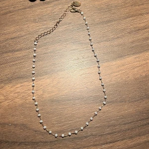 Elegant pärlhalsband - Snyggt och stilrent halsband med små vita pärlor på en tunn kedja. Perfekt för att ge en touch av elegans till din outfit. Justerbar längd med en förlängningskedja.