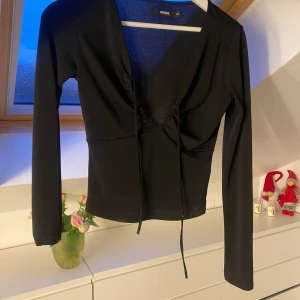 Svart långärmad topp från Bikbok - Snygg svart långärmad topp från Bilbok med v-ringning och knytning framtill. Perfekt för en stilren look.