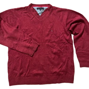 Röd tröja från Tommy Hilfiger - Säljer en snygg röd tröja från Tommy Hilfiger med v-ringning. Tröjan har långa ärmar och ribbade muddar vid ärmslut och nederkant. Perfekt för en stilren look.