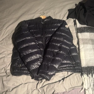 Svart dunjacka från Moncler - Snygg svart dunjacka från Moncler med dragkedja och långärmad design. Perfekt för kyligare väder med sitt pufferstil och högkvalitativa material. Ny pris 12000 storlek 6 som motsvara M skick 9/10 