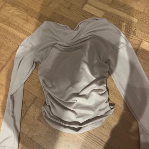 Beige långärmad topp - Säljer en stilren beige långärmad topp med rynkade detaljer på sidorna. Perfekt för en elegant och avslappnad look.