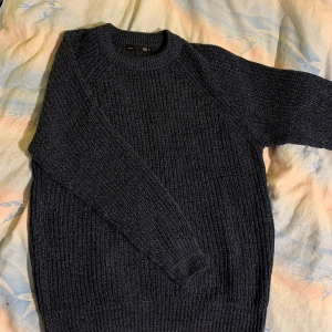 Mörkblå stickad tröja - Säljer en stilren mörkblå stickad tröja med rund hals och långa ärmar. Perfekt för kyliga dagar och passar bra till både jeans och chinos. Tröjan har en klassisk design med ribbstickade muddar vid ärmslut och nederkant.