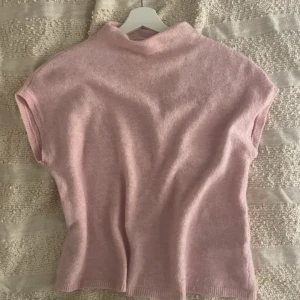 Rosa stickad topp från Lindex - Mysig rosa stickad topp från Lindex med korta ärmar och en hög krage. Perfekt för kyligare dagar när du vill ha något bekvämt och stilrent. Passar bra till både jeans och kjol.